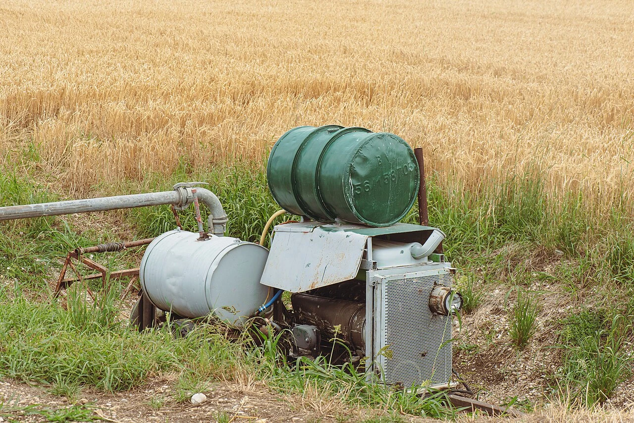 Irrigation pump positioned beside a field with a pipe running away from it